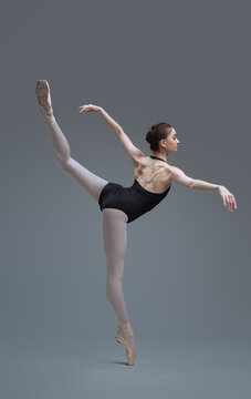 Graceful ballerina staying on one leg inside studio