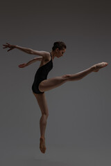 Sideview shot of jumping ballerina against gray background