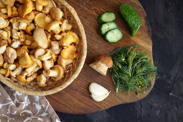 Fototapeta premium mushrooms chanterelles in a basket cucumbers on the table on a dark background