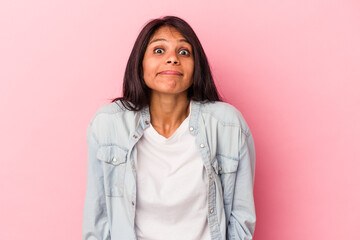Young latin woman isolated on pink background shrugs shoulders and open eyes confused.