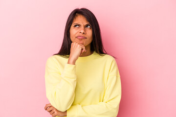 Young latin woman isolated on pink background looking sideways with doubtful and skeptical expression.