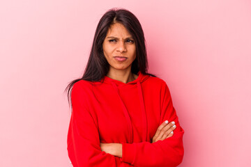 Young latin woman isolated on pink background frowning face in displeasure, keeps arms folded.