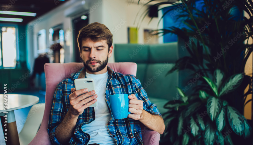 Poster millennial caucasian man with coffee cup checking account balance via banking application on mobile 