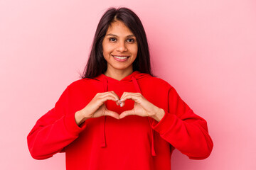 Young latin woman isolated on pink background smiling and showing a heart shape with hands.