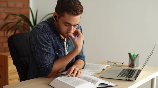 Close-up of concentrated handsome young man student sitting at table and flipping pages of book. Handsome guy educated alone with textbook, searching idea in encyclopedia turning pages