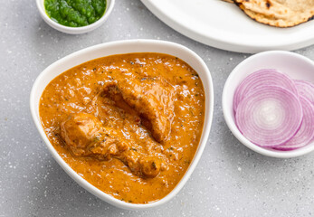 butter chicken gravy served in a white bowl with flatbread roti or naan