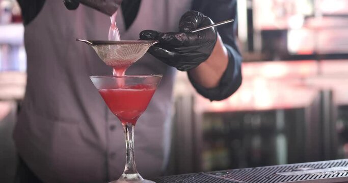 Close up of classy expert bartender making and serving red color cocktail with lime at night club or bar