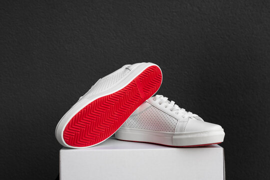 White sneakers with red sole on the box at black background
