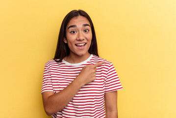 Obraz premium Young mixed race woman isolated on yellow background smiling and pointing aside, showing something at blank space.