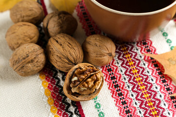 A cup of black tea on a table with an embroidered tablecloth, dry yellowed leaves of a plane tree and walnuts