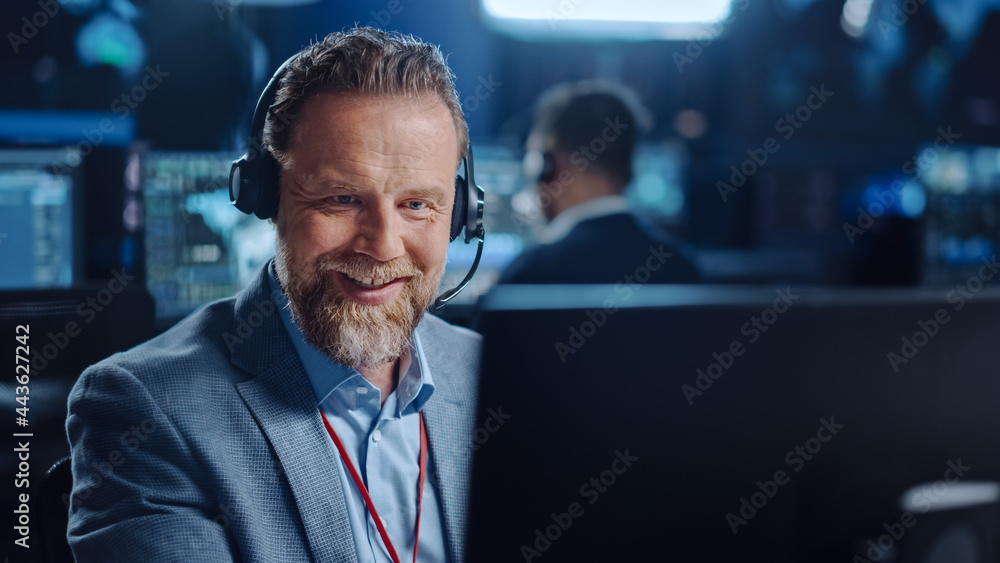 Aufkleber Bearded Happy Senior Technical Support Specialist is Talking on a Headset while Working on a Computer in a Dark Monitoring and Control Room Filled with Computer Display Screens and Data Servers.