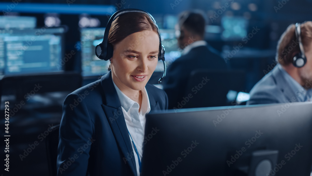 Aufkleber Joyful Beautiful Technical Customer Support Specialist is Talking on a Headset while Working on a Computer in a Dark Monitoring and Control Room Filled with Colleagues and Display Screens.