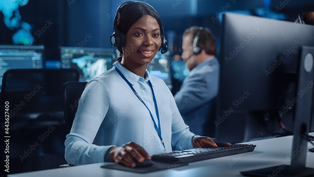 Poster Joyful Beautiful Technical Customer Support Specialist is Talking on a Headset while Working on a Computer in a Call Center Control Room Filled with Colleagues, Display Screens and Data Servers.