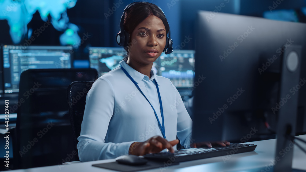 Poster Joyful Beautiful Technical Customer Support Specialist is Talking on a Headset while Working on a Computer in a Call Center Control Room Filled with Colleagues, Display Screens and Data Servers.