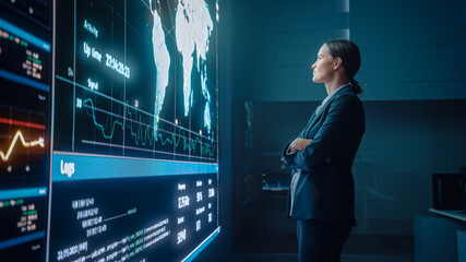 Young Female Computer Science Engineer Looking at Big Screen Display Showing Global Map with Data...