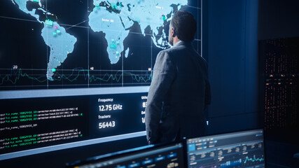 Middle Aged Bearded Senior Project Manager Stands Next to Big Screen with Neural Network. Professional Computer Data Science Engineer Work in a System Control and Monitoring Telecommunications Office.