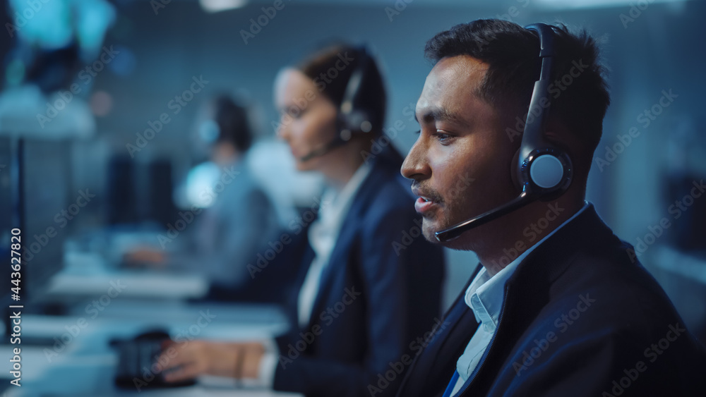 Poster Close Up Portrait of a Joyful Technical Customer Support Specialist Talking on a Headset while Working on a Computer in a Call Center Control Room Filled with Computer Display Screens and Data Servers