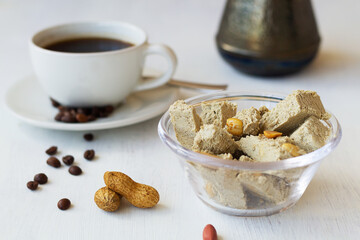 cutting halwa from sunflower seeds with peanut in the glass bowl. national traditional sweetness of Turkish and arabic halva with cup of coffee on the white table. tasty dessert. copy space