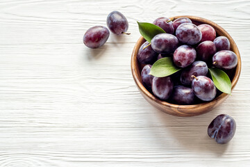 Ripe garden plums in bowl. Cherry fruit with leaves. Top view