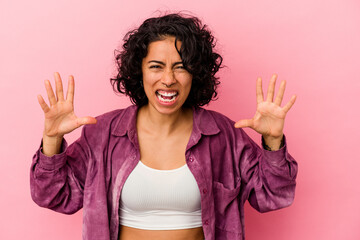 Young curly latin woman isolated on pink background screaming with rage.