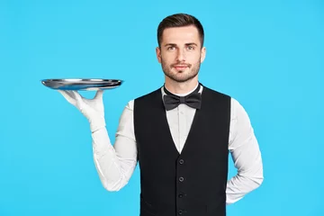 Foto op Plexiglas Attractive young waiter holding empty silver tray over blue background © GVS