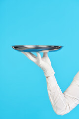Elegant waiter's hand in white glove holding metal tray on blue background.
