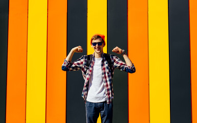 Young excited man, making a winner gesture with raised hands, smiling and shouting about success, against the background of the city colorful wall