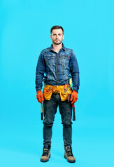 Full length portrait of handsome young male construction worker staying over blue background