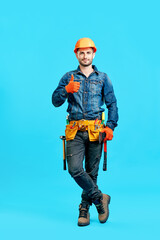 Full length portrait of confident handsome male construction worker in safety helmet showing thumbs...