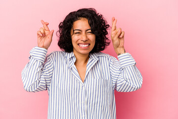 Young curly latin woman isolated on pink background crossing fingers for having luck