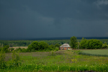 Obraz premium Lonely Ukrainian brick rural house in the distance against the background of meadows, fields, forests and black rain clouds