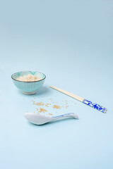 Bowl of blue rice with white and blue chopstick, white and blue spoon with scattered sesame seeds on endless blue background