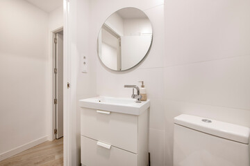Fototapeta na wymiar Apartment toilet with round mirror, white sink, white furniture and white painted walls