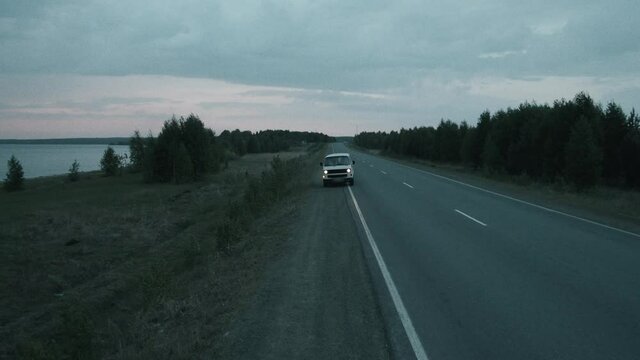 High angle wide shot of camper van riding towards the camera and stopping at side of road in dusk