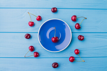 Top view flat lay red cherries and blue plate.