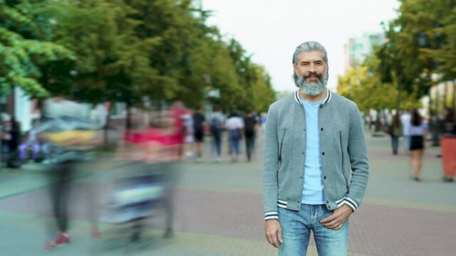 Time lapse of handsome bearded man standing outdoors in crowded pedestrian street with people walking around. City life and society concept.