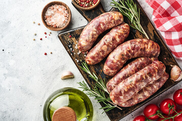 Raw sausages or bratwurst on cutting board with spices and ingredients for cooking. Top view with copy space on light grey stone table.