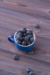 Top view pile of blueberries in a blue ceramic cup on wooden background.