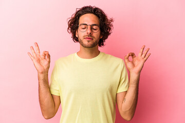 Young caucasian man isolated on pink bakcground relaxes after hard working day, she is performing yoga.