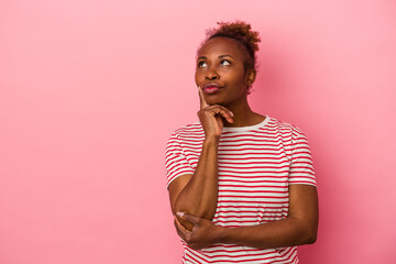 Young african american woman isolated on pink background looking sideways with doubtful and skeptical expression.