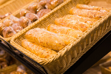 Fototapeta premium fresh golden breads with melted cheese wrapped in plastic wrap in wicker basket in bread department of supermarket
