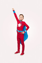 Positive boy in superhero costume standing in studio with raised arm