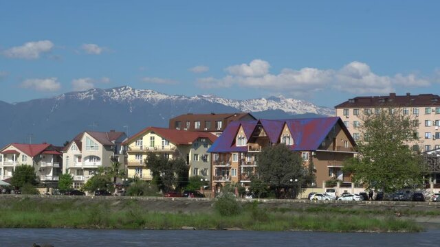 Residential buildings in federal territory of Sirius against backdrop of snow-capped peaks. Caucasus mountains. Imeretinskaya lowland. In foreground is Mzymta.Adler. Sochi, Russia - May 18, 2021