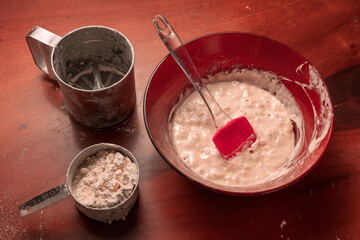 Yeast bread dough in a bowl and a cup of flour with flour sieve on table