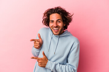 Young caucasian man isolated on pink bakcground excited pointing with forefingers away.