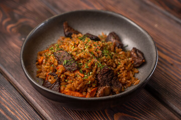 Traditional pilaf with meat in a black plate on a wooden background