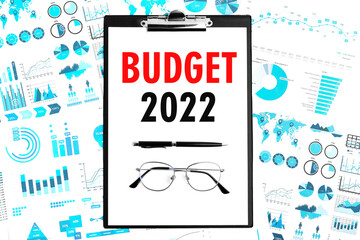 Text BUDGET 2022 on clipboard. Pen and glasses on clipboard with charts, documents and graphs....
