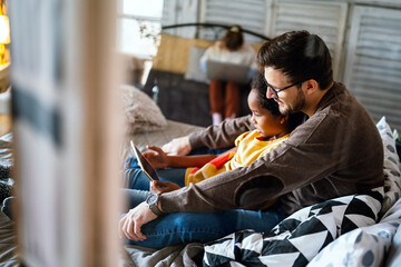 Multiethnic father and child using electronic tablet at home. Technology, education, people concept
