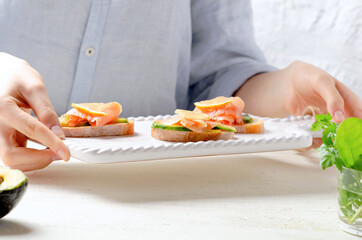 Young girl holds tray with fresh salmon and avocado on white bread. 