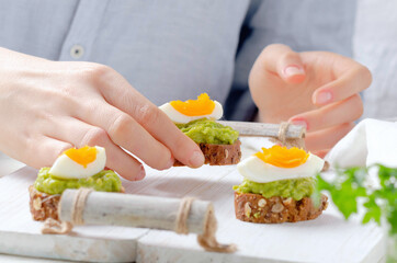 Female hand holds sandwich of avocado cream with egg on light background.